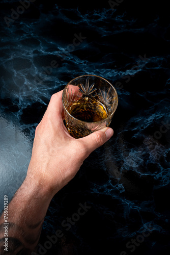hand holding and grabbing whisky glass on dark marble table in studio environment