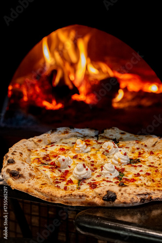 Pizza topped with creamy ricotta coming out of a wood fired oven
