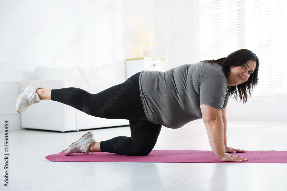 Fototapeta premium Overweight woman in sportswear stretching on yoga mat at home