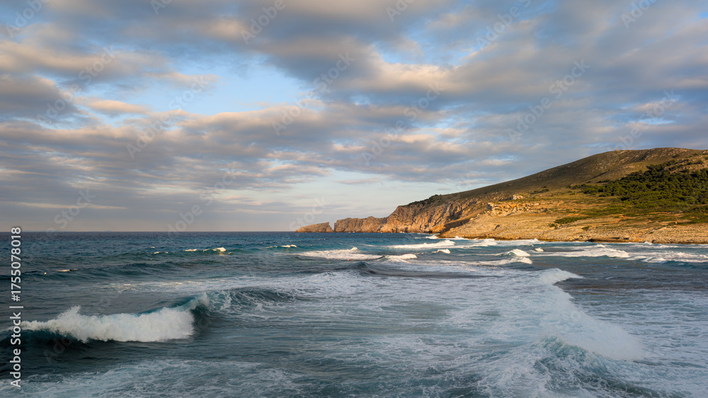 Obraz premium Horizontal photo of stormy sea waves rolling into a bay surrounded by green mountains under a cloudy sky. Dramatic ocean landscape with moody weather and powerful nature energy. Perfect for travel