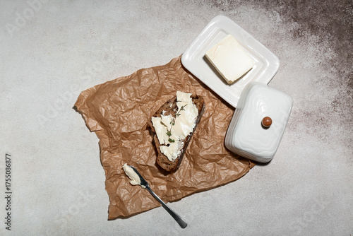 Slice of fresh bread with butter and knife on grey grunge background