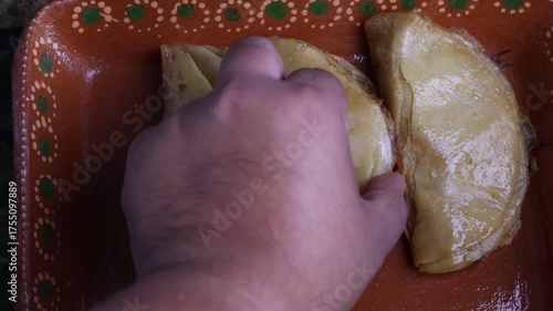 Hands preparing delicious traditional steamed tacos with spicy red sauce in a clay dish