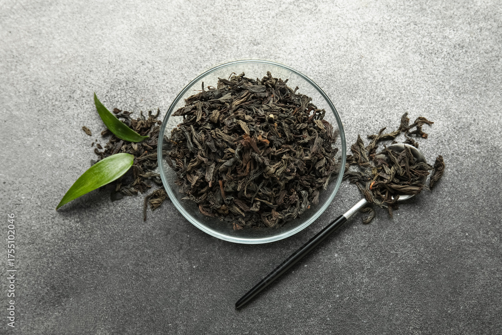Fototapeta premium Bowl of dry black tea leaves with spoon on white background