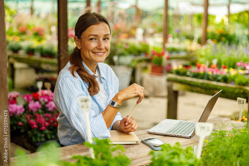 A joyful woman is happily engaging with her laptop while surrounded by vibrant flowers in a lovely garden center