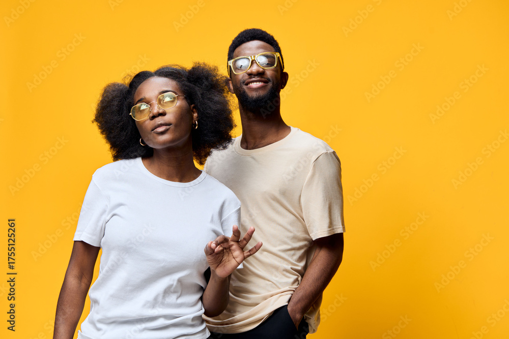Fototapeta premium Stylish African American couple posing playfully in trendy outfits against a vibrant yellow background, showcasing confidence and happiness