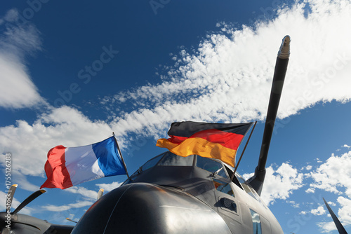 Military airplane and aircraft with two wavy national flags of Germany and France. German and French air force. Alliance of European allies and armed forces and defense. Blue sky as copy space
