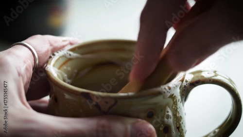Close-up shot of a person's hand stirring a drink inside a ceramic mug with a wooden stick.