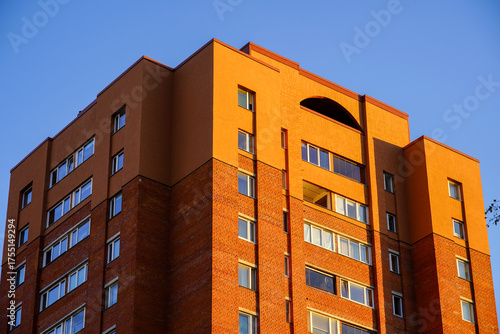 Modern orange brick apartment building under clear blue sky at sunset in a city neighborhood