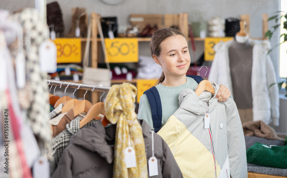 Naklejka premium Smiling adolescent female customer holding a hanger with puffer jacket during sale in retail outlet