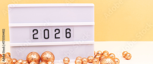 Lightbox with 2026 numbers and sparkly balls in front of golden background. Festive New Year concept with copy space.