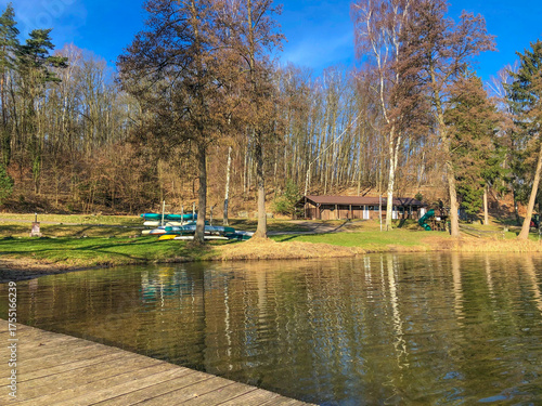 Idyllischer See mit Bootshaus und Kanus im Sonnenschein, umgeben von Bäumen und klarem Wasser. Perfekte Landschaftsidylle für Freizeit, Natur und Erholung.