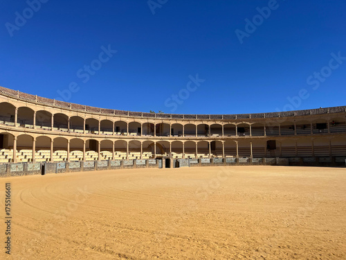 Historische Stierkampfarena in Ronda, Spanien, unter klarem blauem Himmel. Antike Architektur mit Rundbögen und Sandplatz, typisches Beispiel andalusischer Kultur und Geschichte.