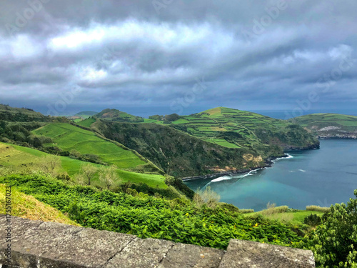Grüne Küstenlandschaft mit terrassierten Hügeln und Blick auf das Meer unter dramatisch bewölktem Himmel – friedliche Naturidylle auf einer atlantischen Insel