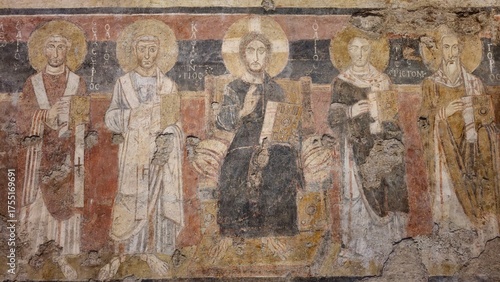 Rome, Italy - 13 January 2025. In Santa Maria Antiqua, a worn fresco depicts Christ between four saints, all with halos and gospel books, set against a red and black background.