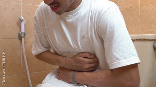 Man sitting on toilet holding stomach in pain