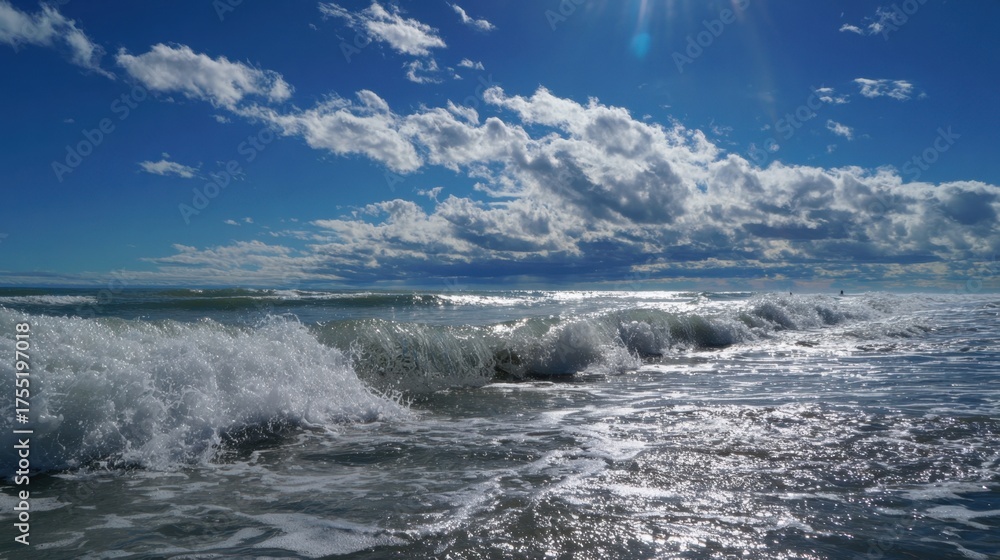 Fototapeta premium Bright sunlight sparkles on the ocean waves as they crash softly on the shore creating a calm scene.