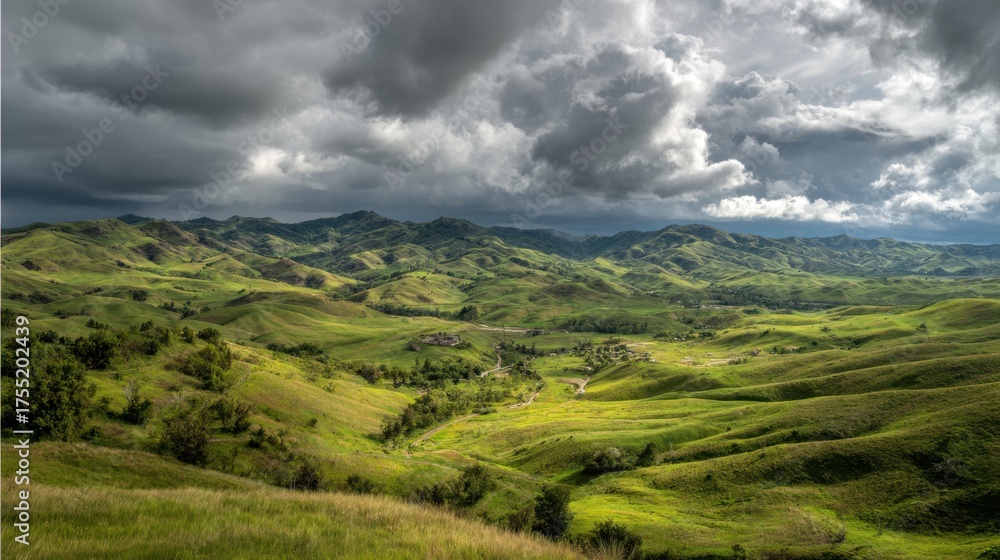 Obraz premium A sweeping view of green hills and valleys unfolds beneath an overcast sky filled with dramatic clouds.