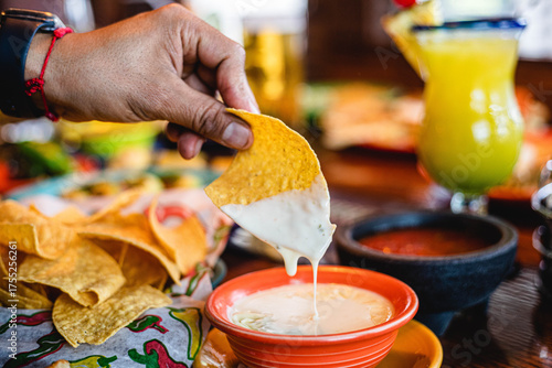 Fotografia hand dipping a tortilla chip in queso cheese dip at a Mexican restaurant