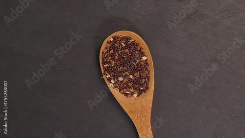 Overhead shot showcases colourful array of spices herbs on a wooden spoon pach phoron clove cardamom black seed salt pepper table spread of on dark black slate board