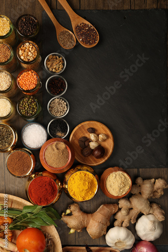 Overhead flat lay vibrant colourful spices herbs fresh produce vegetables legumes on wooden table spread splash smoking spice mix dark black slate metal clay pot palm leaf plate board copy text frame