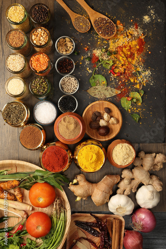 Overhead flat lay vibrant colourful spices herbs fresh produce vegetables legumes on wooden table spread splash smoking spice mix dark black slate metal clay pot palm leaf plate board copy text frame