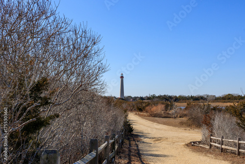 View of a tall lighthouse from a sandy path surrounded by bare trees on a clear day