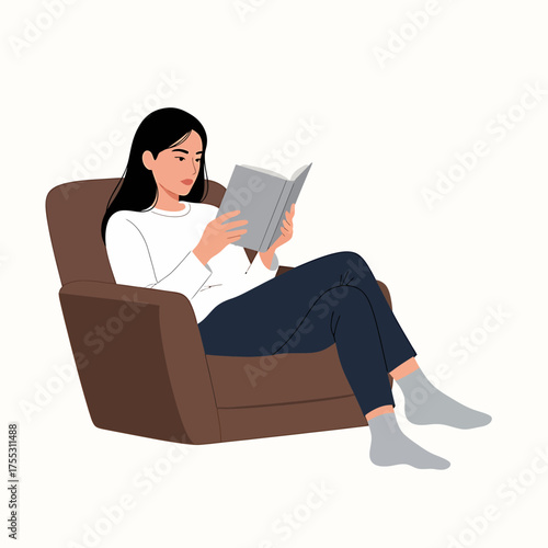 A woman is sitting comfortably in an armchair, engrossed in reading a book.