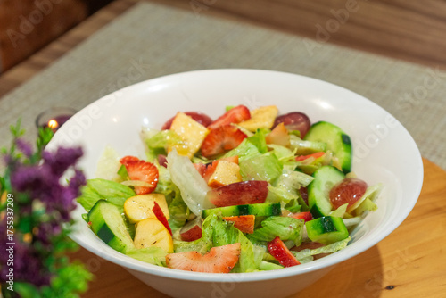 Photograph of a homemade salad with fruits and vegetables placed on a white plate on a round wooden plate