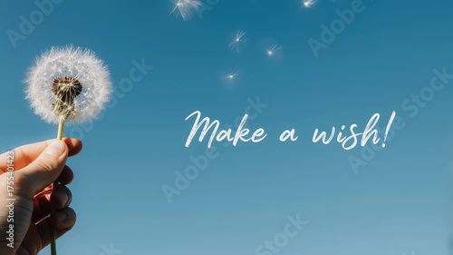 Hand holding dandelion with floating seeds against a bright blue sky and text 