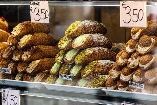 A tempting window display of stacked Sicilian Cannoli pastries in Venice, featuring classic, pistachio, and amaretto flavors, with handwritten price tags showcasing Italian street food.

