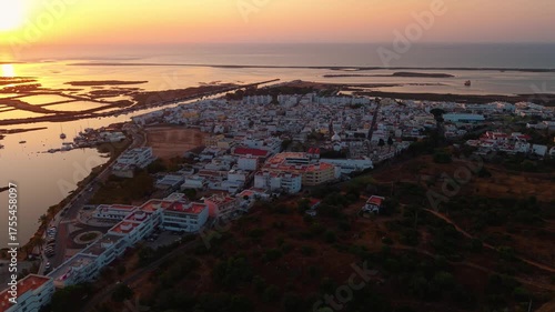 aerial shot above Fustea fishing village at sunrise near Ria Formosa natural park in Algarve region with the village in the foreground and the salt pans in the background, Portugal