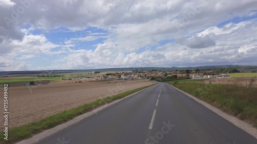 Reims, Marne, Grand-Est, France, August, 28th, 2025, Champagne Area, A picturesque view of a rural road leading into a vibrant village with expansive fields under a cloudy sky.