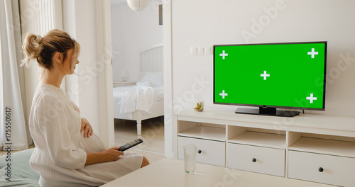 фотографія Pregnant woman with remote control watching chroma key tv while sitting on coffee table at home