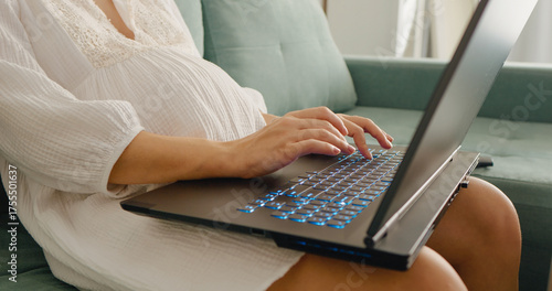 Midsection shot of unrecognizable pregnant woman working on laptop placed on laps doing paperwork at home.. Pregnant woman working at computer. Freelance and remote work.