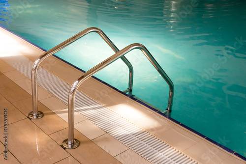 Stainless steel pool ladder, deck and turquoise water pool.