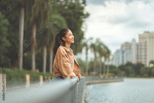 Fotografie Beautiful Asian woman relaxing by riverside in city park, smiling female enjoyin