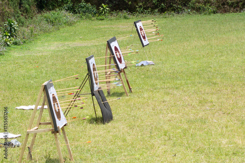 An open grassy field with multiple archery targets arranged in a row and trees in the distance.