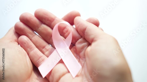Close-up of female hand holding pink satin ribbon, symbolizing support for breast cancer awareness, medical care, and self-examination.