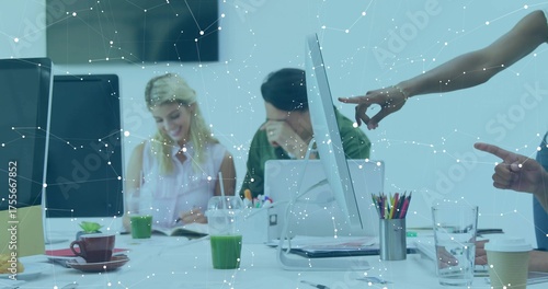 Collaborating colleagues reviewing documents around table in office with monitors and green juice