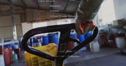 Gloved hand guiding pallet jack through warehouse, with red drums, yellow crates and code overlay