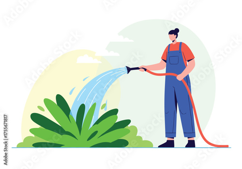 A person in overalls waters green plants with a hose.