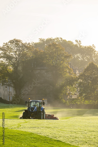 Fotografie Tractor lawnmower cutting grass in city park early in the morning