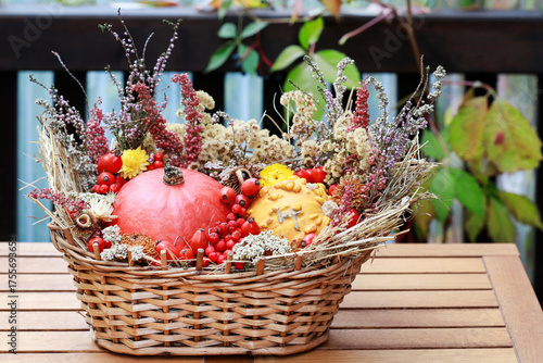 Florist at work: woman shows how to make seasonal autumn table decoration with pumpkins, flowers and plants in a wicker basket.