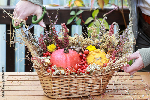 Florist at work: woman shows how to make seasonal autumn table decoration with pumpkins, flowers and plants in a wicker basket.
