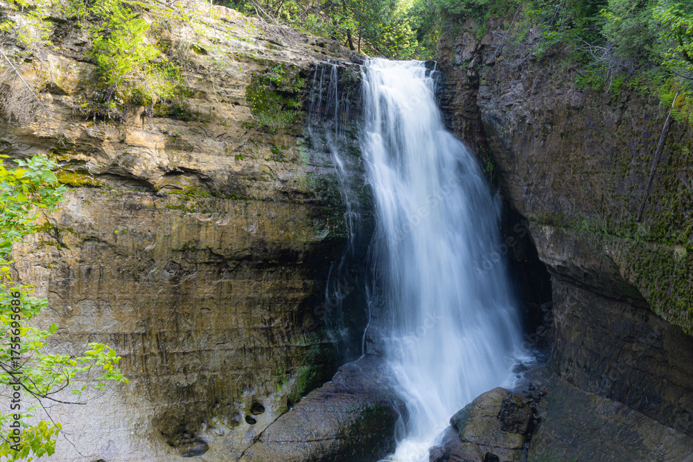 Obraz premium Waterfall cascading over rock ledge in forest