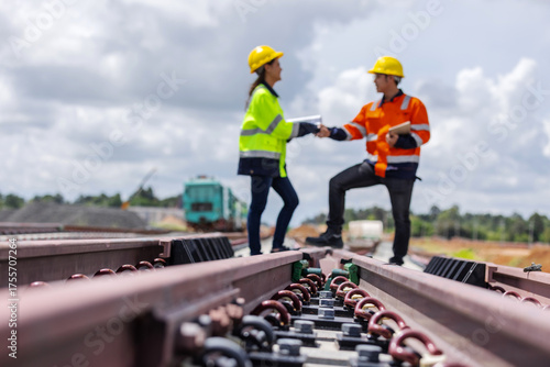 Two construction engineers wearing safety helmets and high-visibility jackets shaking hands on a railway construction site. Teamwork, project agreement, infrastructure development, industrial safety, 