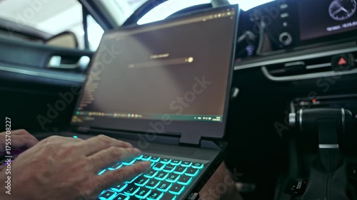 Man typing on laptop computer inside car, concept of remote work and mobility, shallow depth of field with selective focus on hands and keyboard, soft bokeh