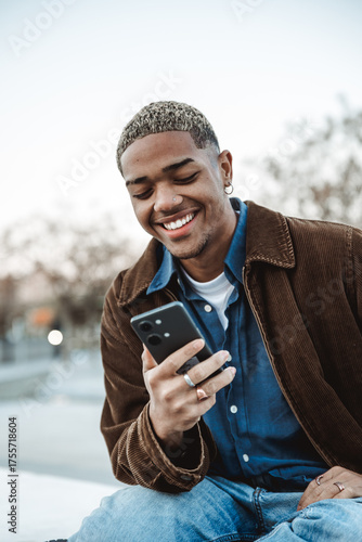Portrait of a smiling young man looking at a mobile phone in a park