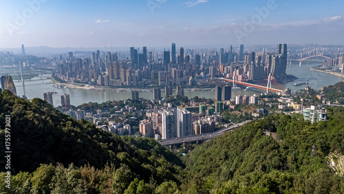 A scenic view of the modern Chongqing skyline seen from a lush, green mountain overlook. The contrast between nature and the dense urban environment is highlighted on a clear day