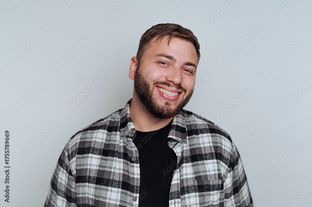 Fototapeta premium Smiling man wearing a plaid shirt poses for a friendly portrait against a light background